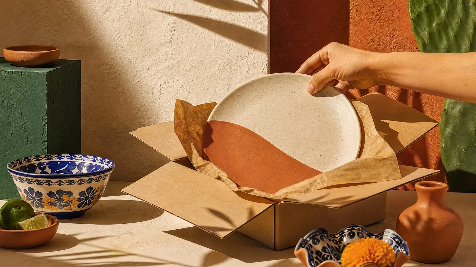 A stoneware plate being lifted from paper wrapping in an open kraft box